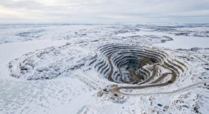 Aerial view of a terraced open-pit mine in a snowy landscape. Spiral roads lead down into the pit, with small vehicles